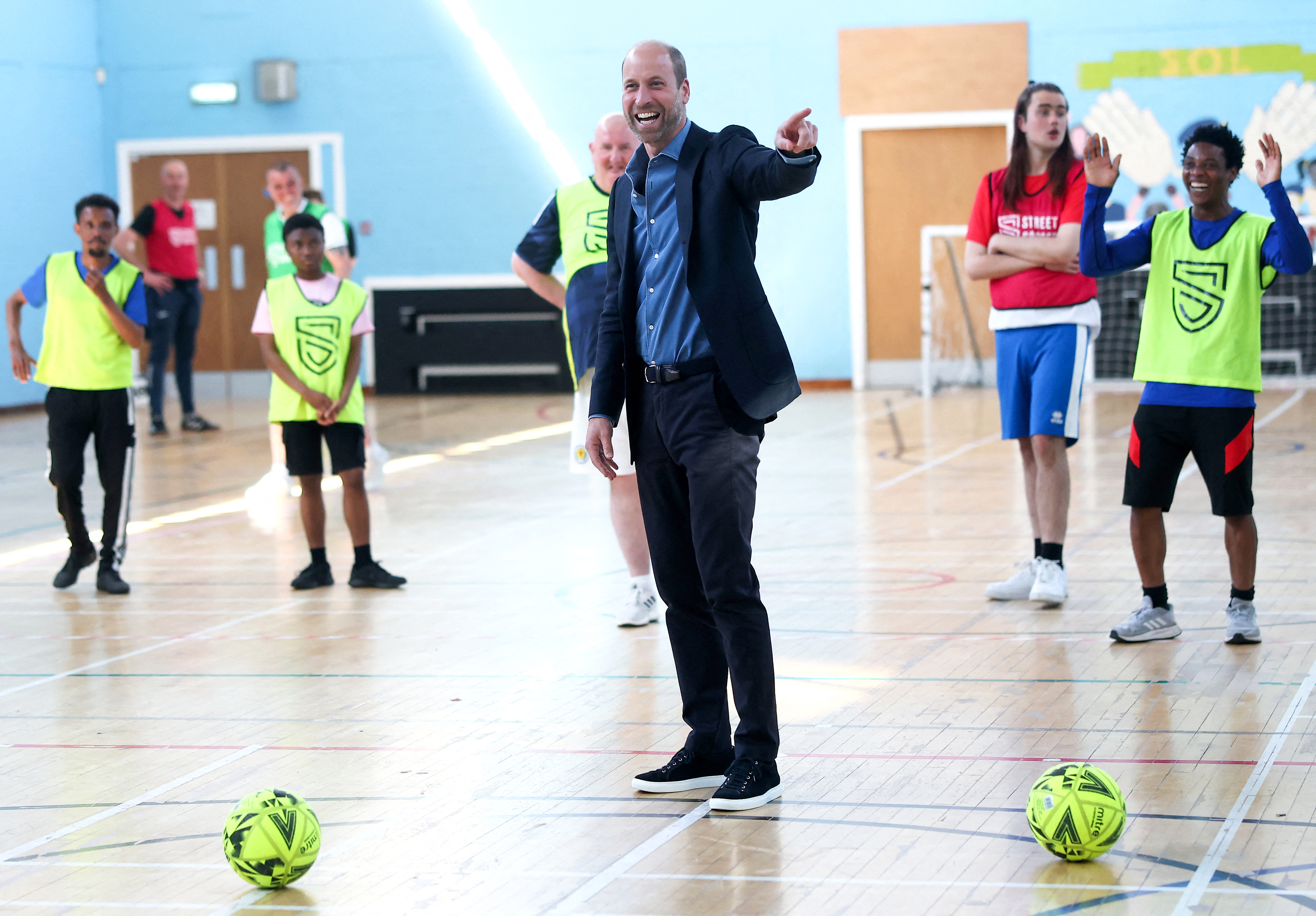 Prince William standing in a gym with soccer balls and laughing