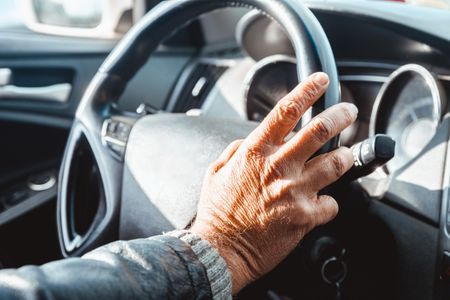 An older man's hand is on the wheel of a car, with the keys in the ignition.