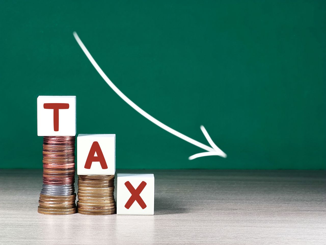 white blocks spelling &quot;tax&quot; on a descending pile of coins with a white arrow going down 