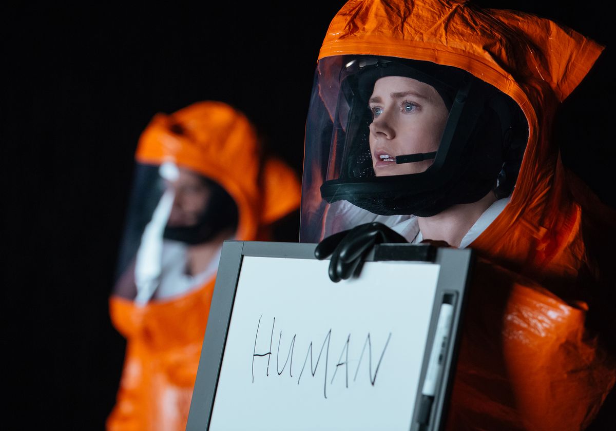 Amy Adams in a hazmat suit holds up a sign which reads &#039;Human&#039;