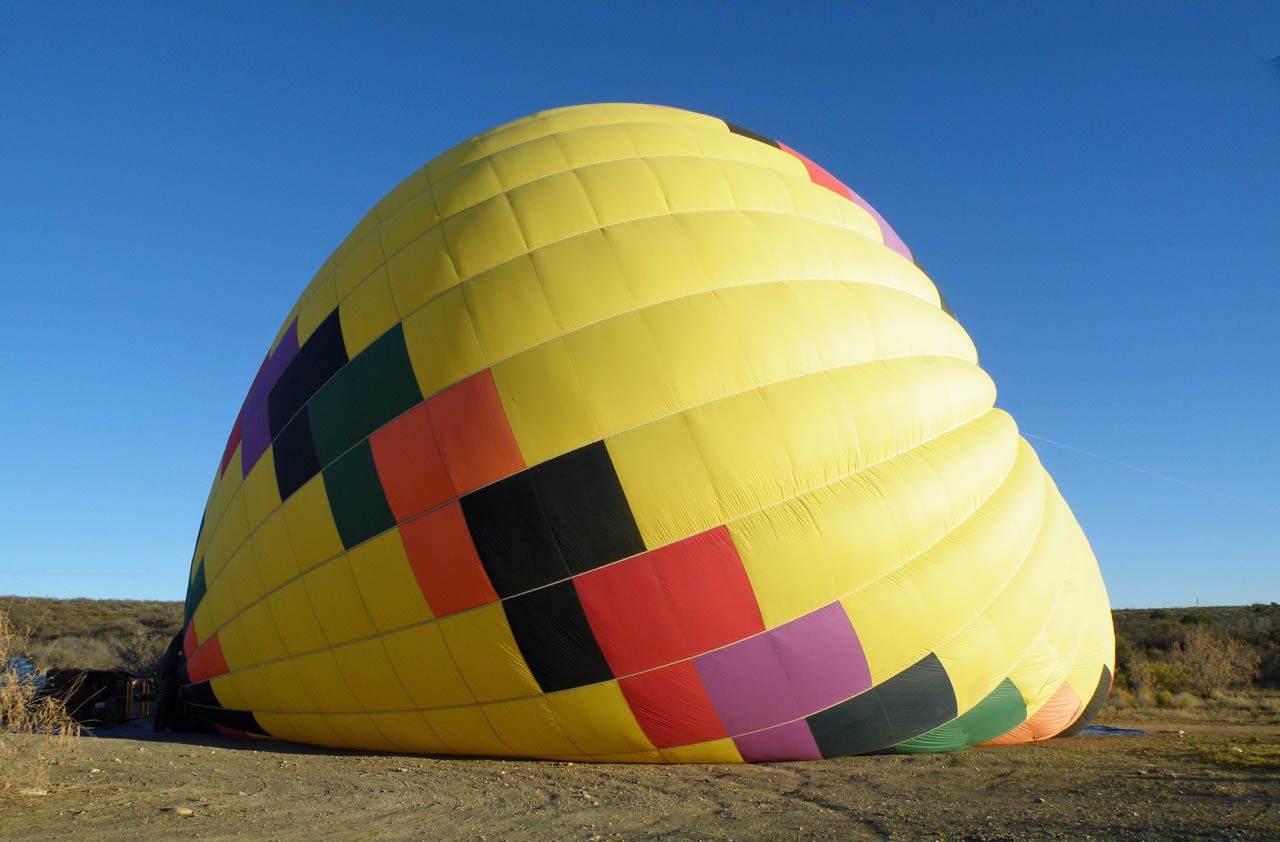 Brightly colored hot airballoon against blue sky. Ballon is partially inflated / deflated