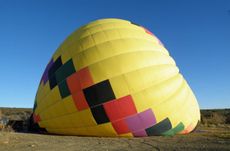 Brightly colored hot airballoon against blue sky. Ballon is partially inflated / deflated