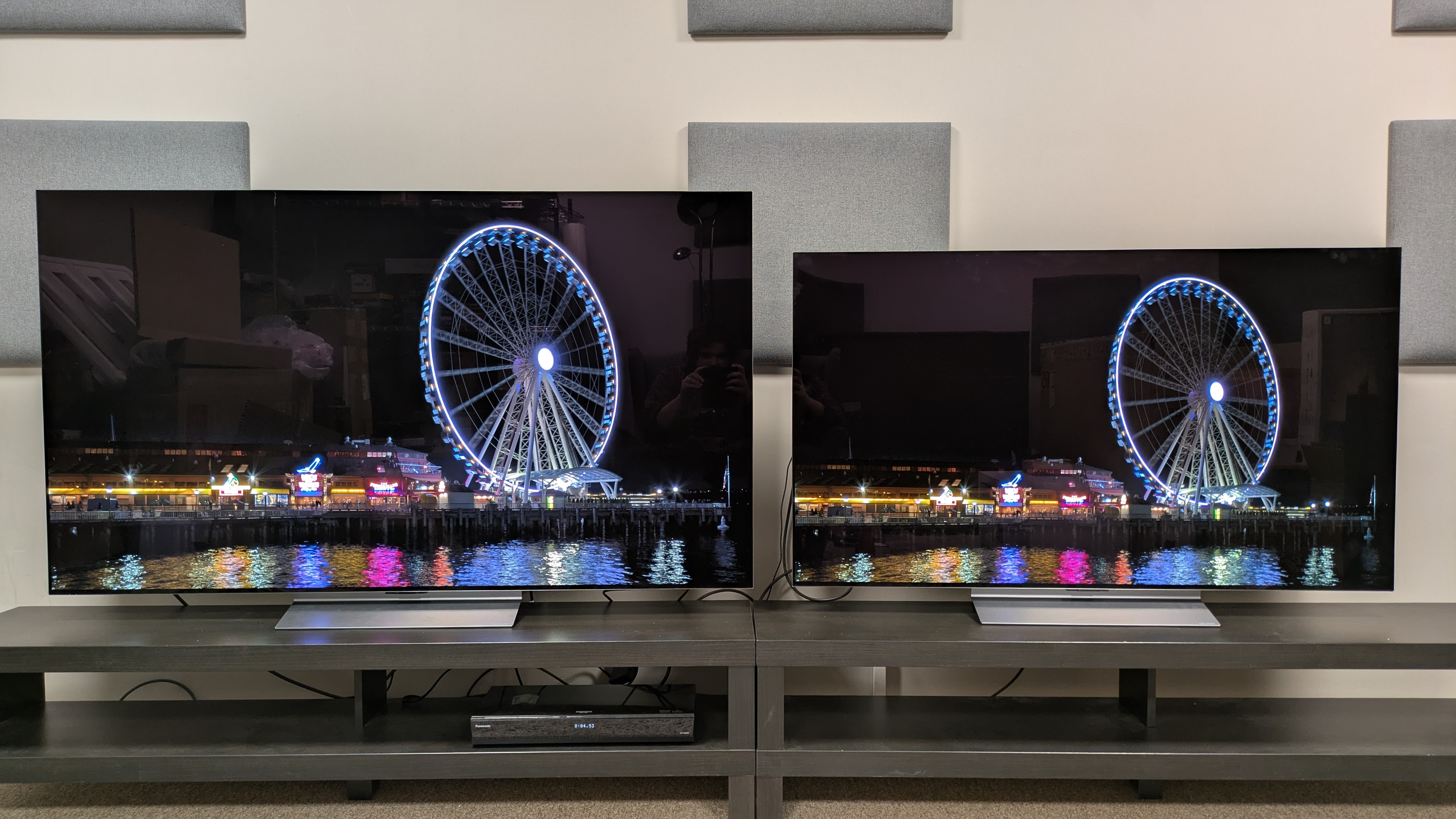 LG C6 (left) and LG C5 (right) with a ferris wheel on a pier at night on screen. Both TVs show great contrast, but lots of mirror like reflections in a bright room