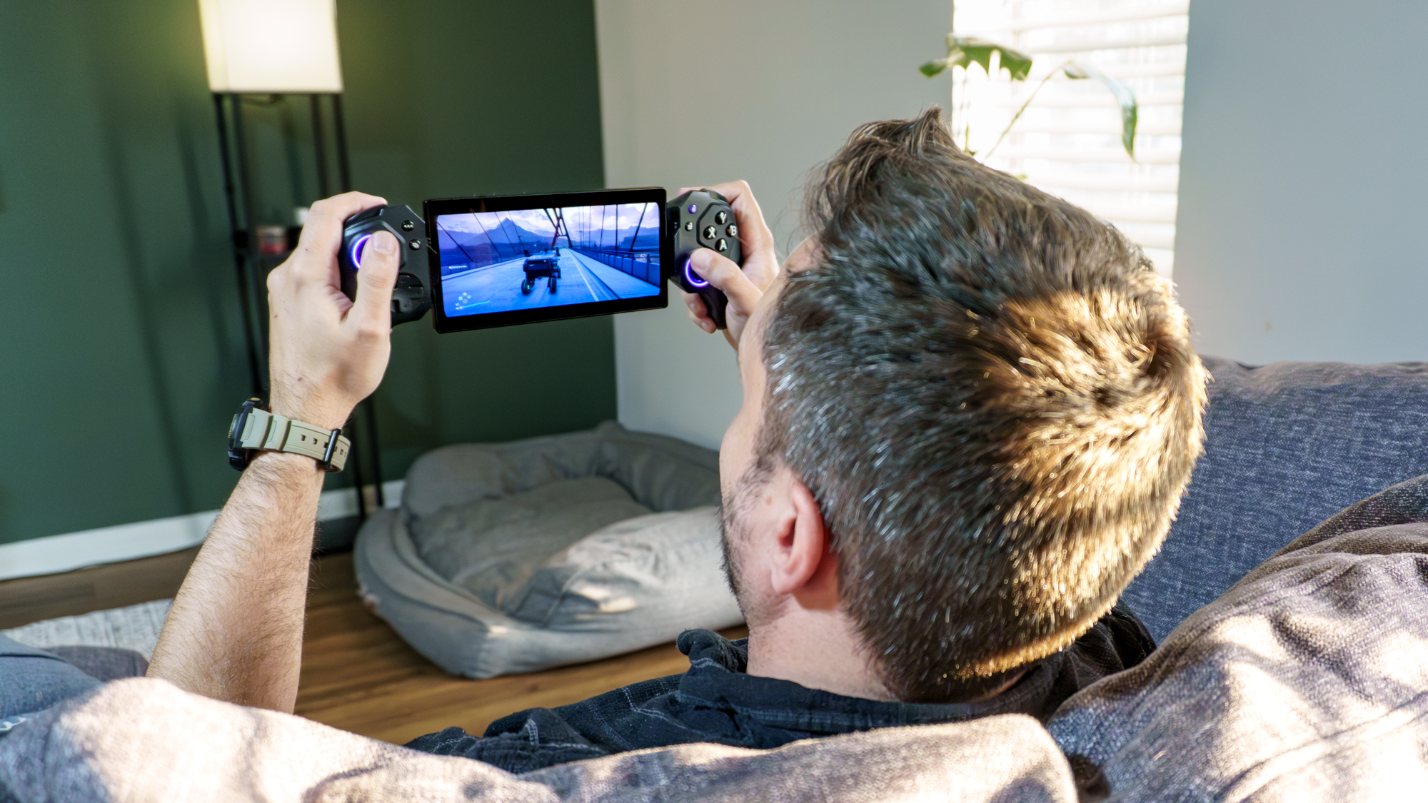A person sitting on the couch playing Death Stranding 2 remotely using the Elo Vagabond mobile game controller