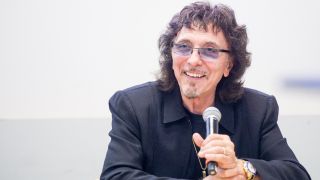 Tony Iommi sat and holding a microphone in 2023