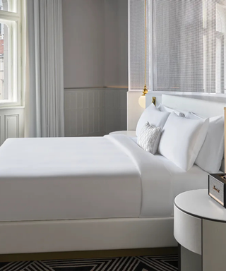 Side view of white bedding on W Hotels Mattress against a white wall.