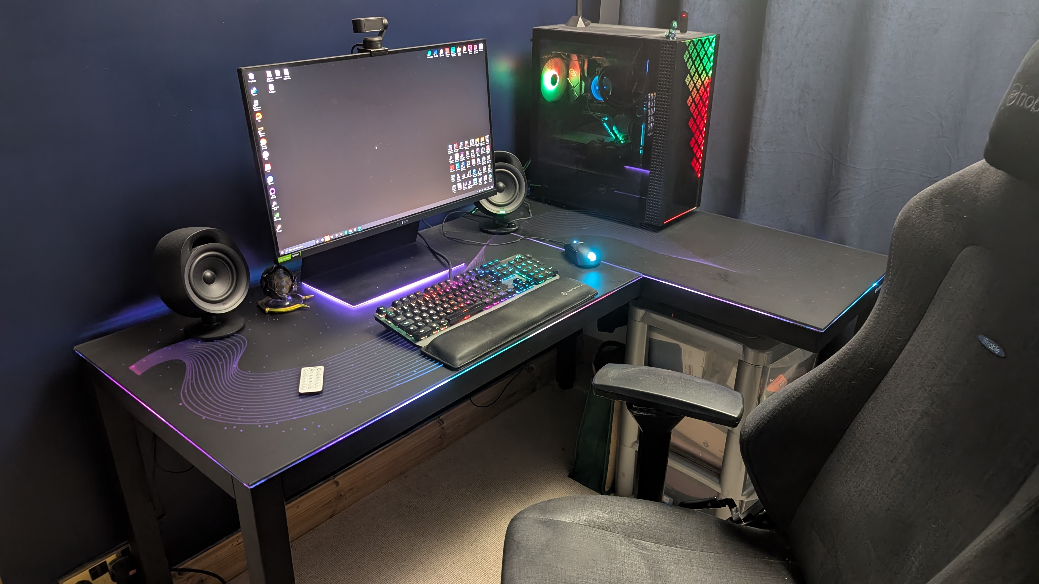 The Eureka Ergonomic GTG Wave gaming desk in a well-lit room with a PC setup on it and a gaming chair in front, with all the RGB lights turned on.