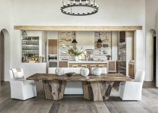 A kitchen extension with a dining table in the middle of the room, with chairs on each side. Above the table is a light fixture.