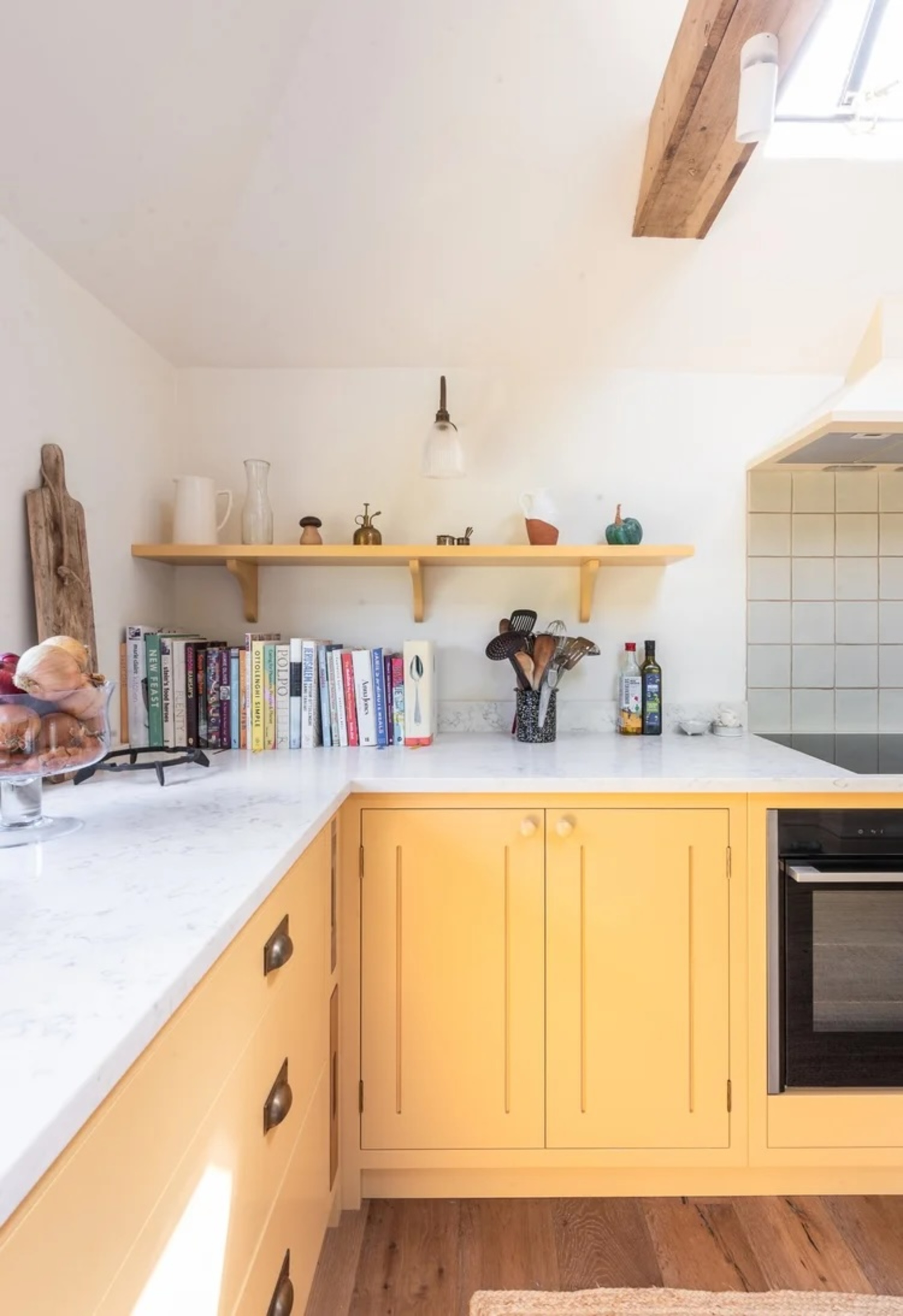 yellow kitchen with shaker joinery, white countertop, and floating shelf with cookbooks stacked underneath and white walls