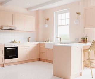 pale peach kitchen units with peach and white striped wallpaper on walls around window and next to breakfast bar