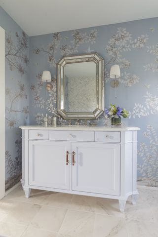 bathroom with blue floral wallpaper, antique mirror, wall lights, white vanity unit, stone floor