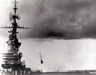 a black and white photo from the deck of an aircraft carrier as a rocket lifts into the sky.