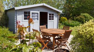 A garden shed with its door open next to a table and chairs