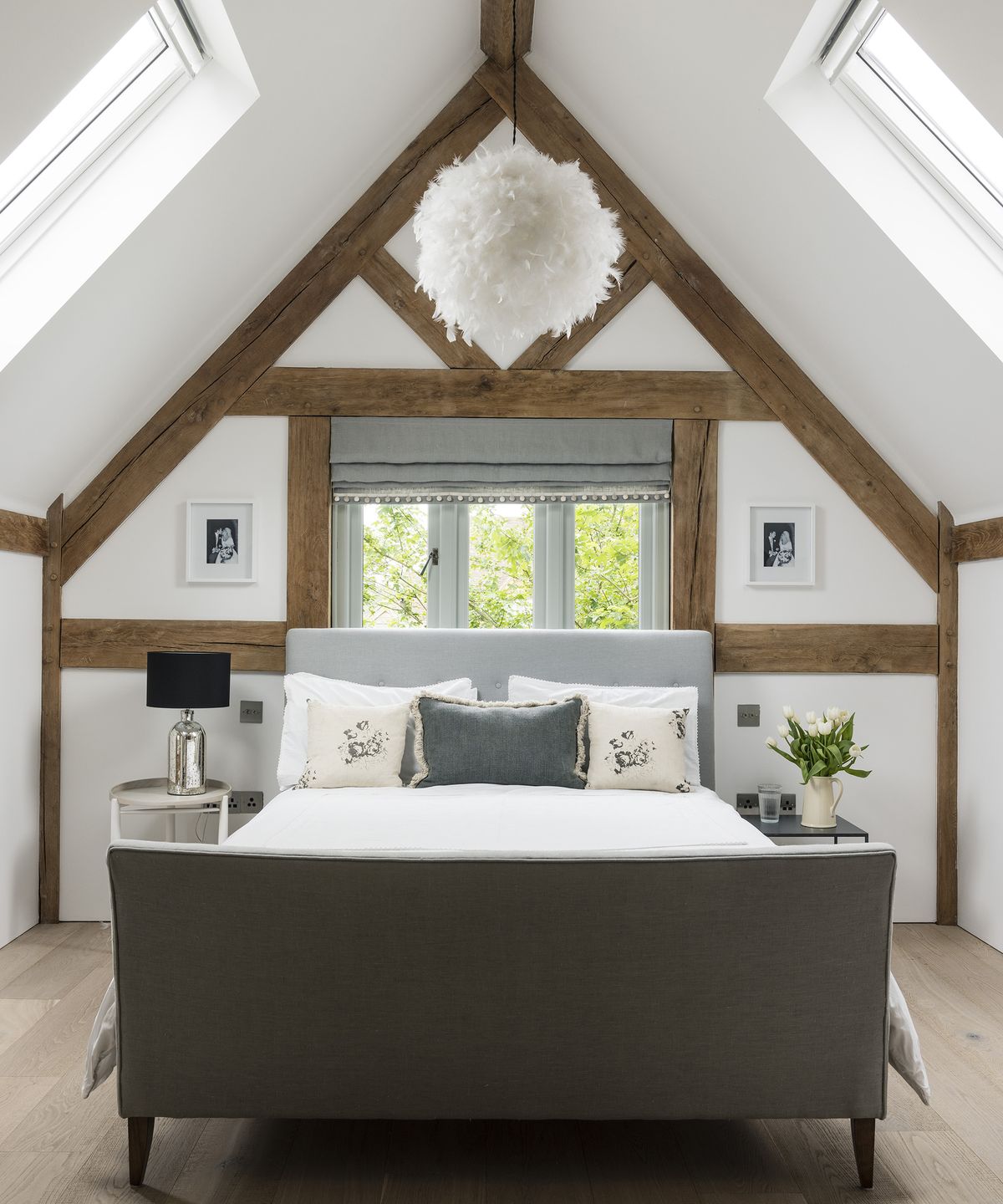 A double bed in the loft portion of an oak frame home. There are exposed beams and neutral walls