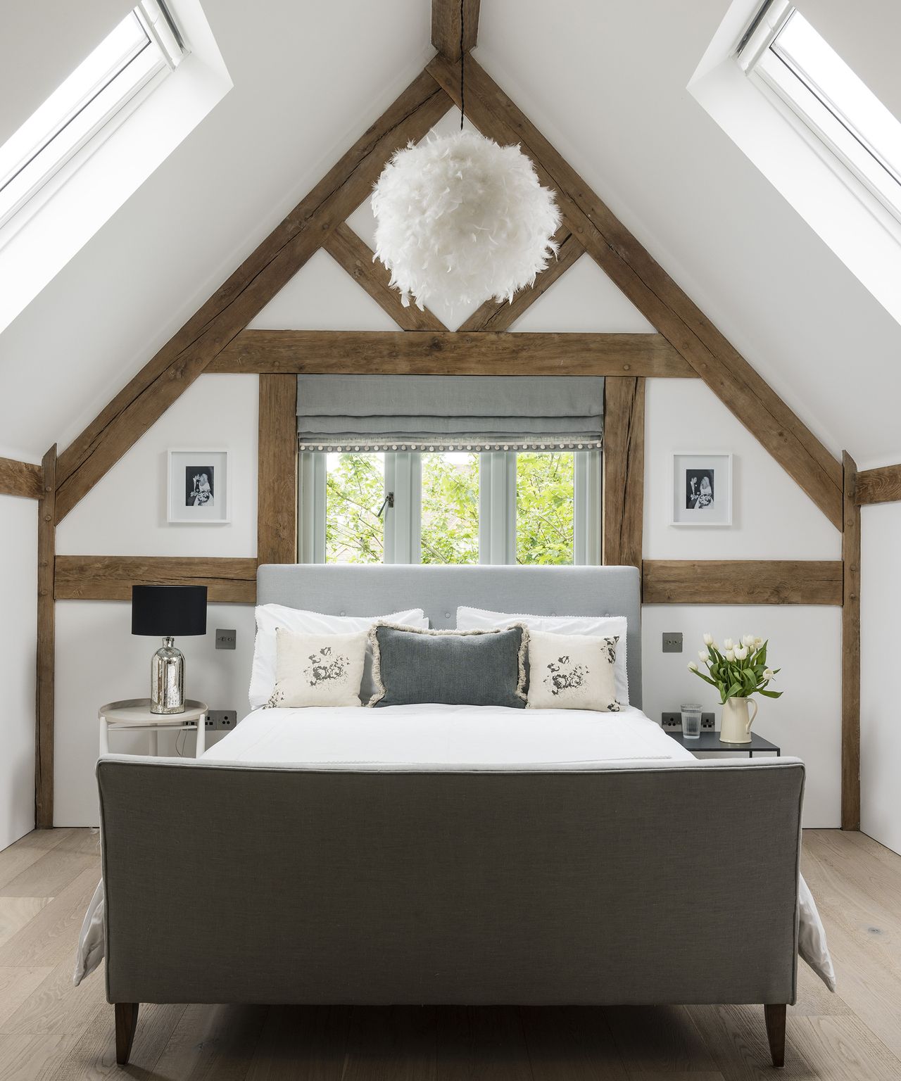 A double bed in the loft portion of an oak frame home. There are exposed beams and neutral walls