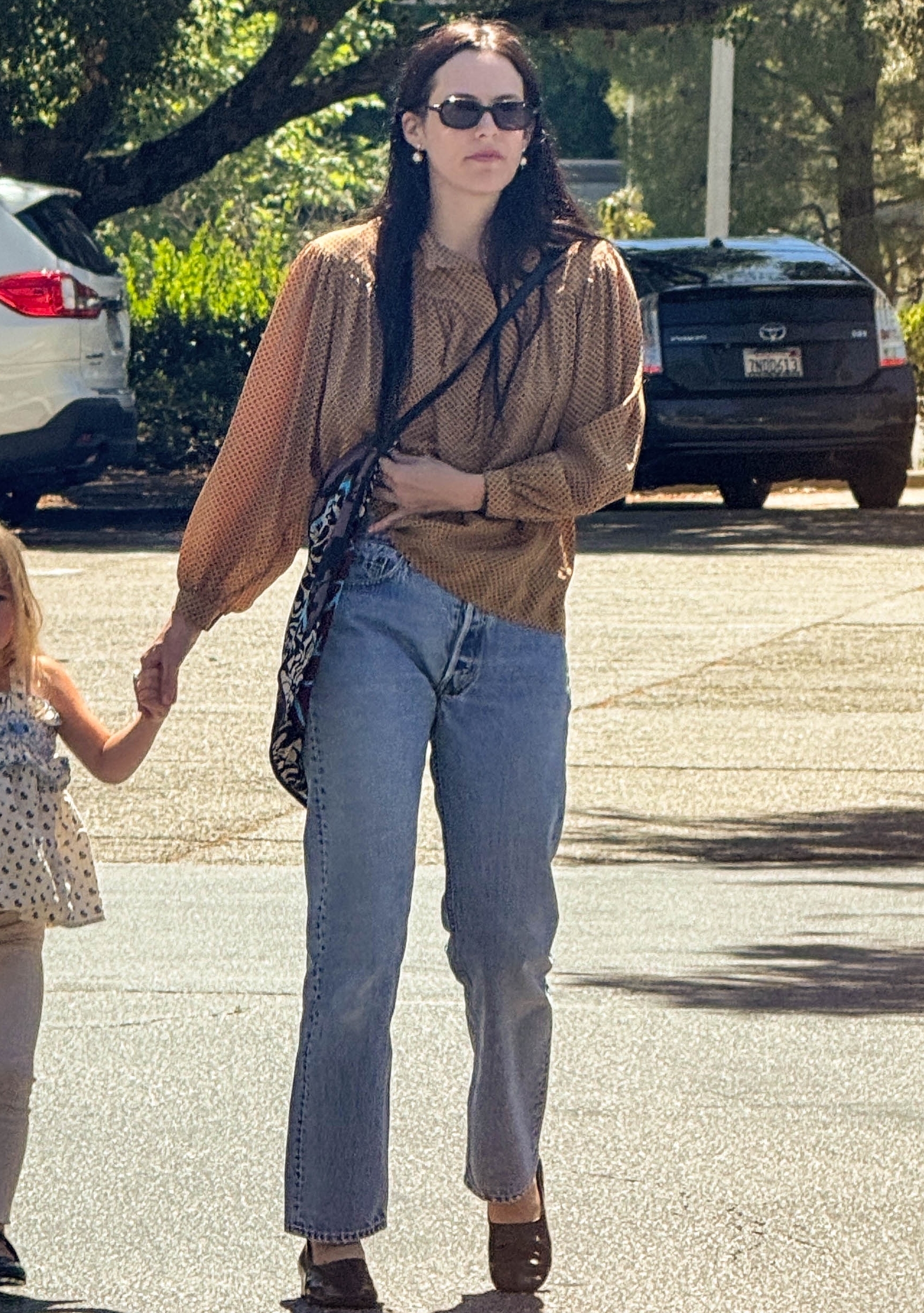 Riley Keough walks down the street wearing straight-leg jeans with a blouse and high-vamp flats.