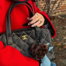 A woman in a red coat holding a Chanel handbag with blue and brown nail art