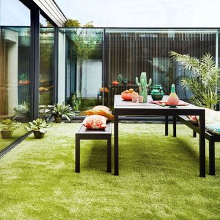 outdoor dining with artificial grass, modern houses, dark wood table and benches, tropical cushions and accessories