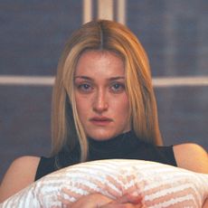 sarah pidgeon as carolyn bessette kennedy crying and hugging a pillow while watching the news about princess diana's death in fx's love story