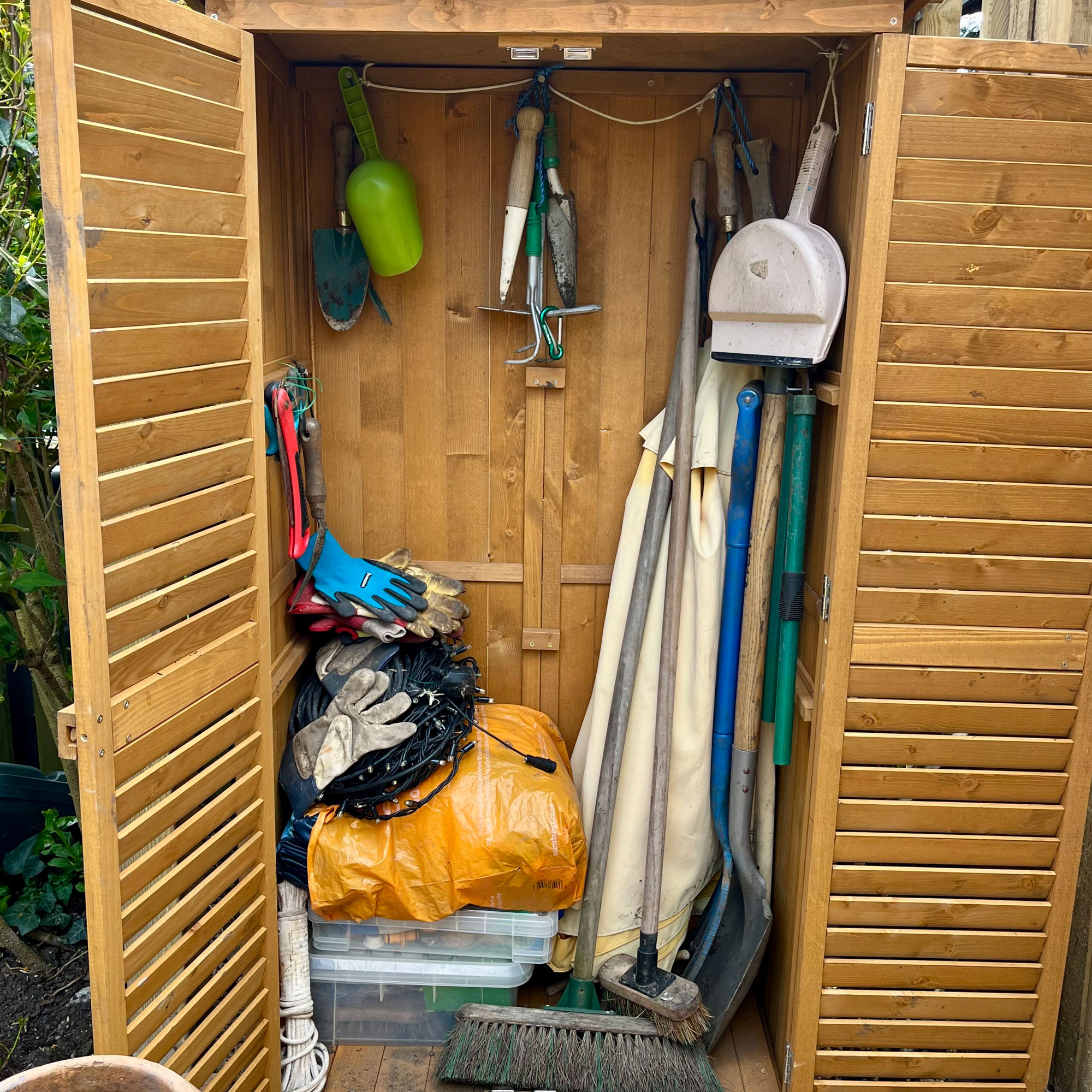 Wooden garden wardrobe in a garden with a wooden fence and pots filled with plants
