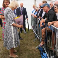 Queen Camilla looking at a man's tattoos in a crowd with a shocked expression 