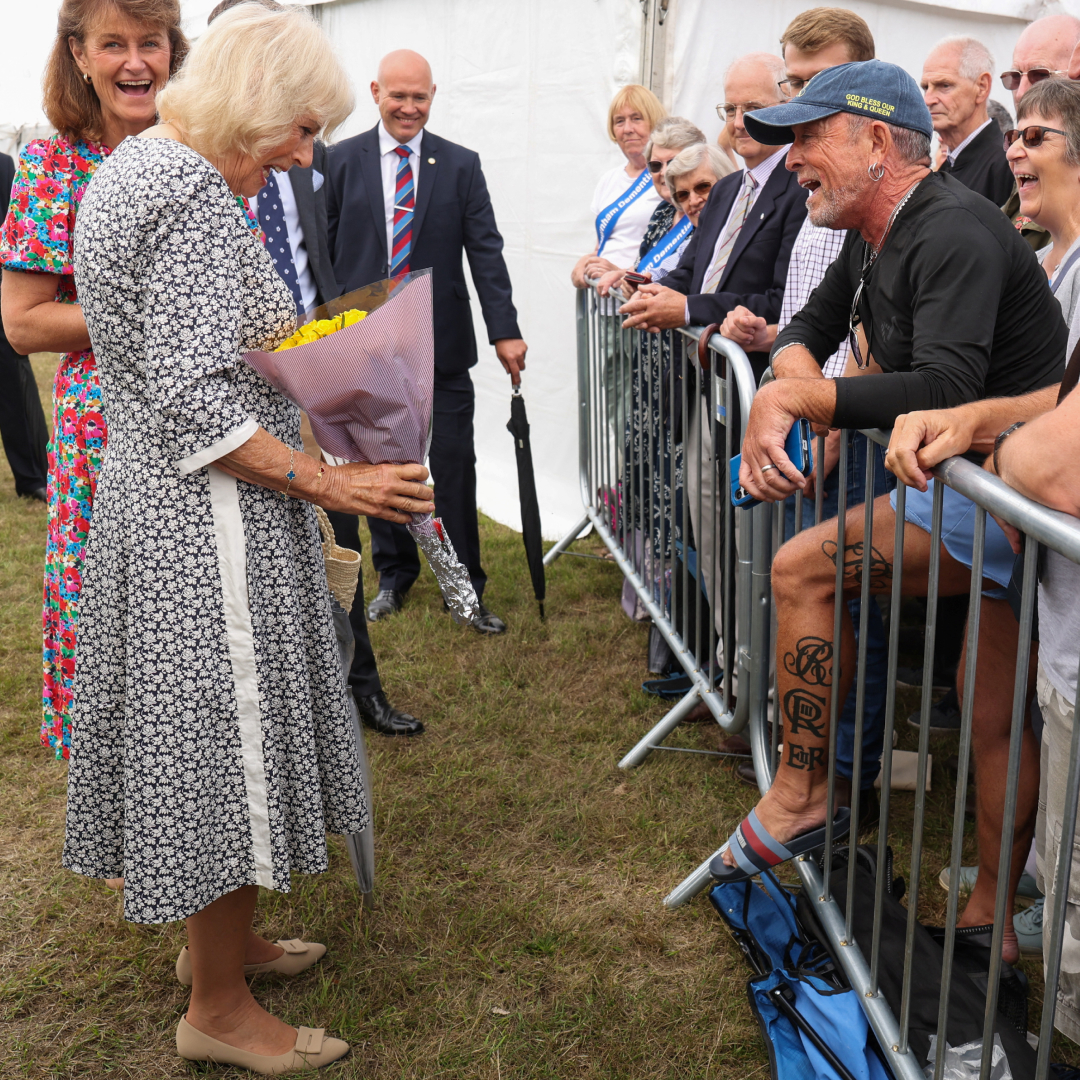 Queen Camilla looking at a man&#039;s tattoos in a crowd with a shocked expression 