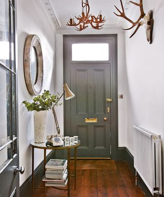 A grey and white hallway with a mirror, statement light and antlers on the wall