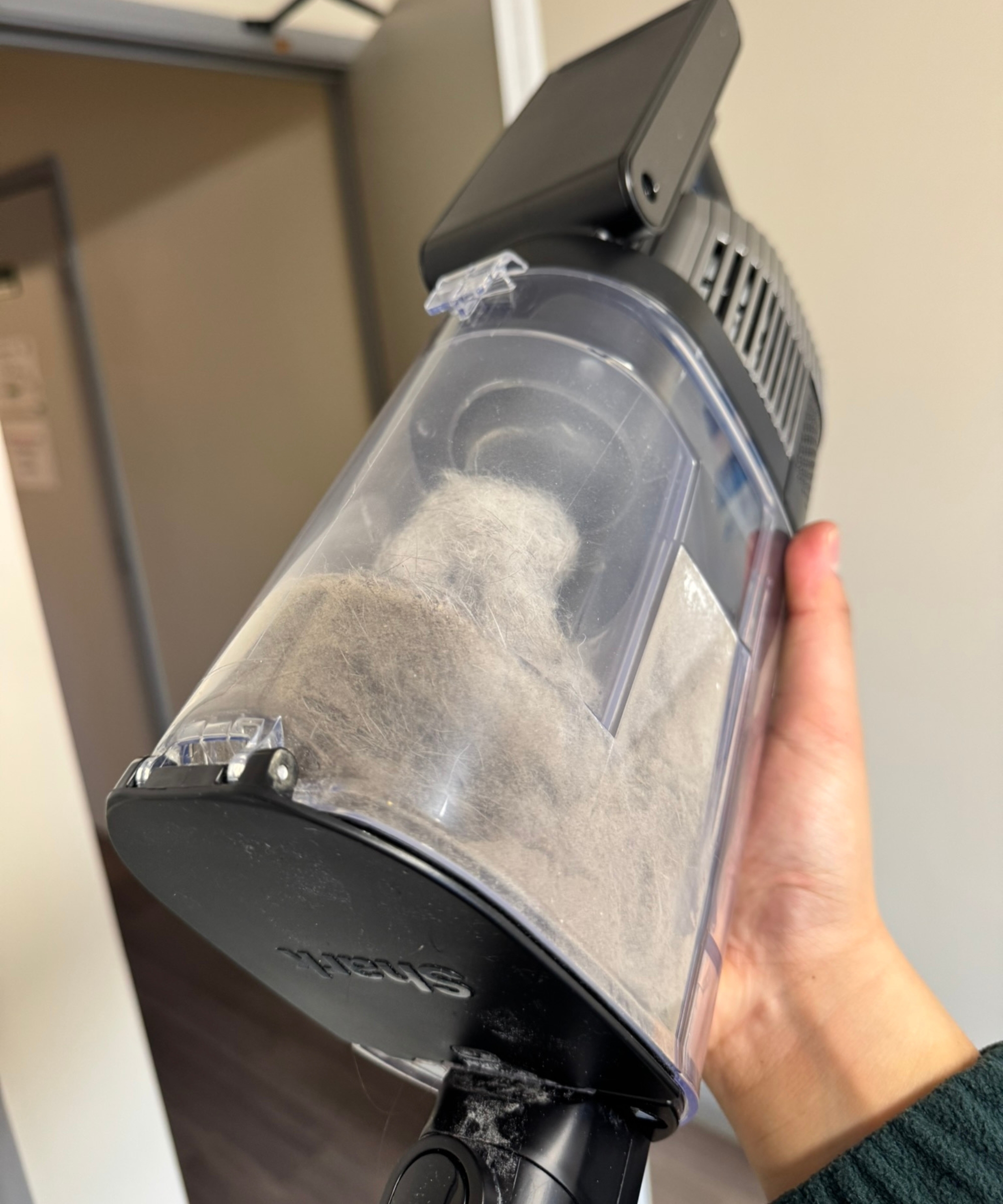 Hand holding the Shark Stratos Cordless, with its dustbin full of pet hair.
