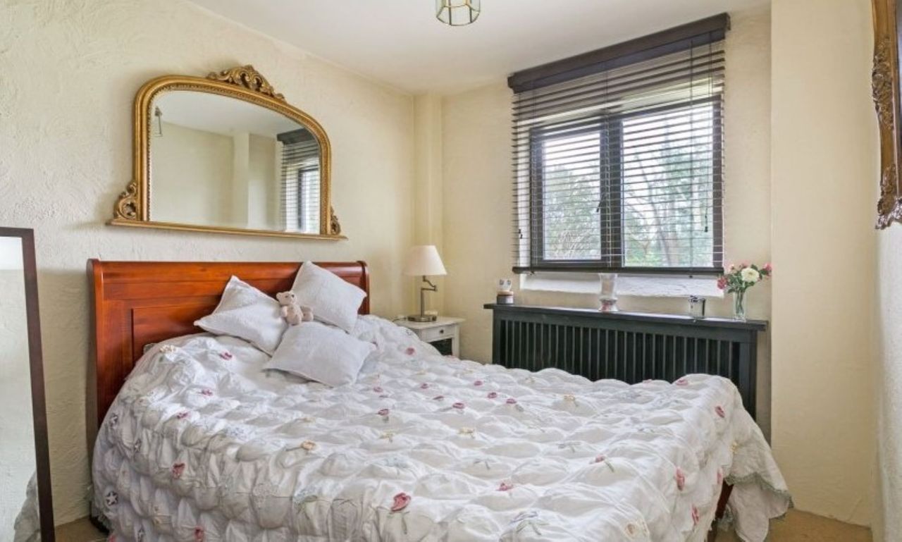 The bedroom has white linen coverings and a brown dressing table underneath the window
