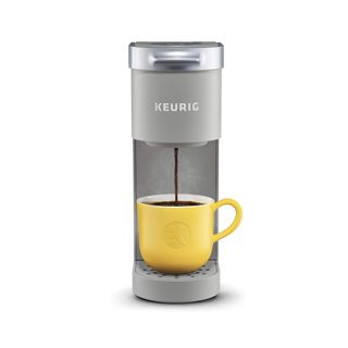 The Keurig K-Mini Coffee Maker in grey brewing coffee into a yellow mug on the cup stand