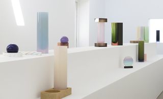 White block platforms with installation of geometric and colourful vessels in enamelled porcelain and iridescent glass objects, white wall background