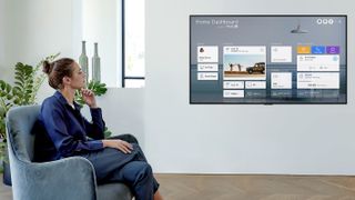 A woman sitting looking at a LG GX wall mounted next to her