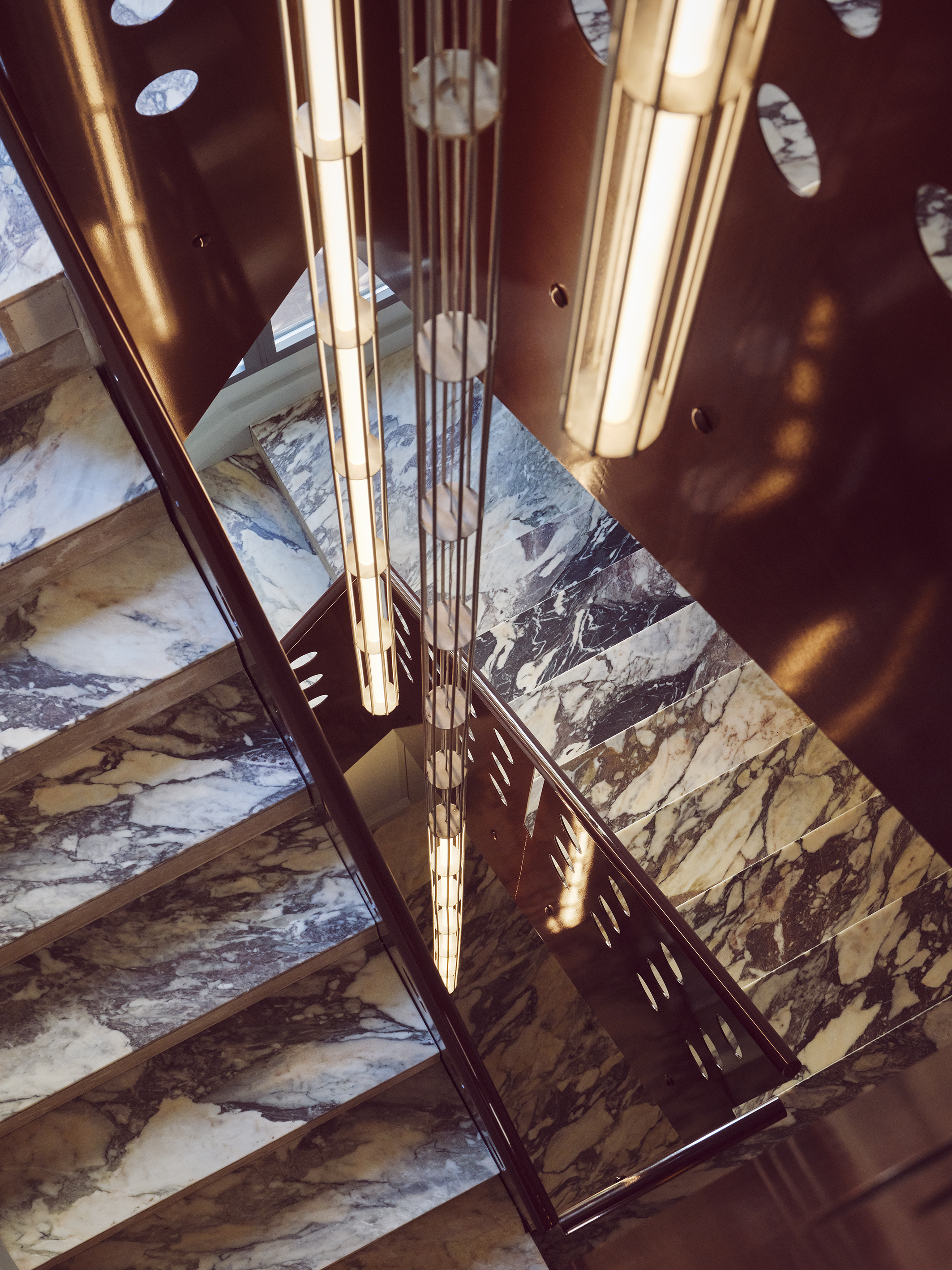 a marble staircase with a long vertical chandelier