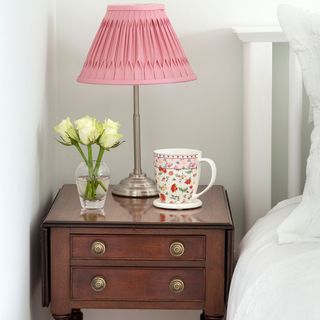 bedside wooden table with pink lamp and flower vase