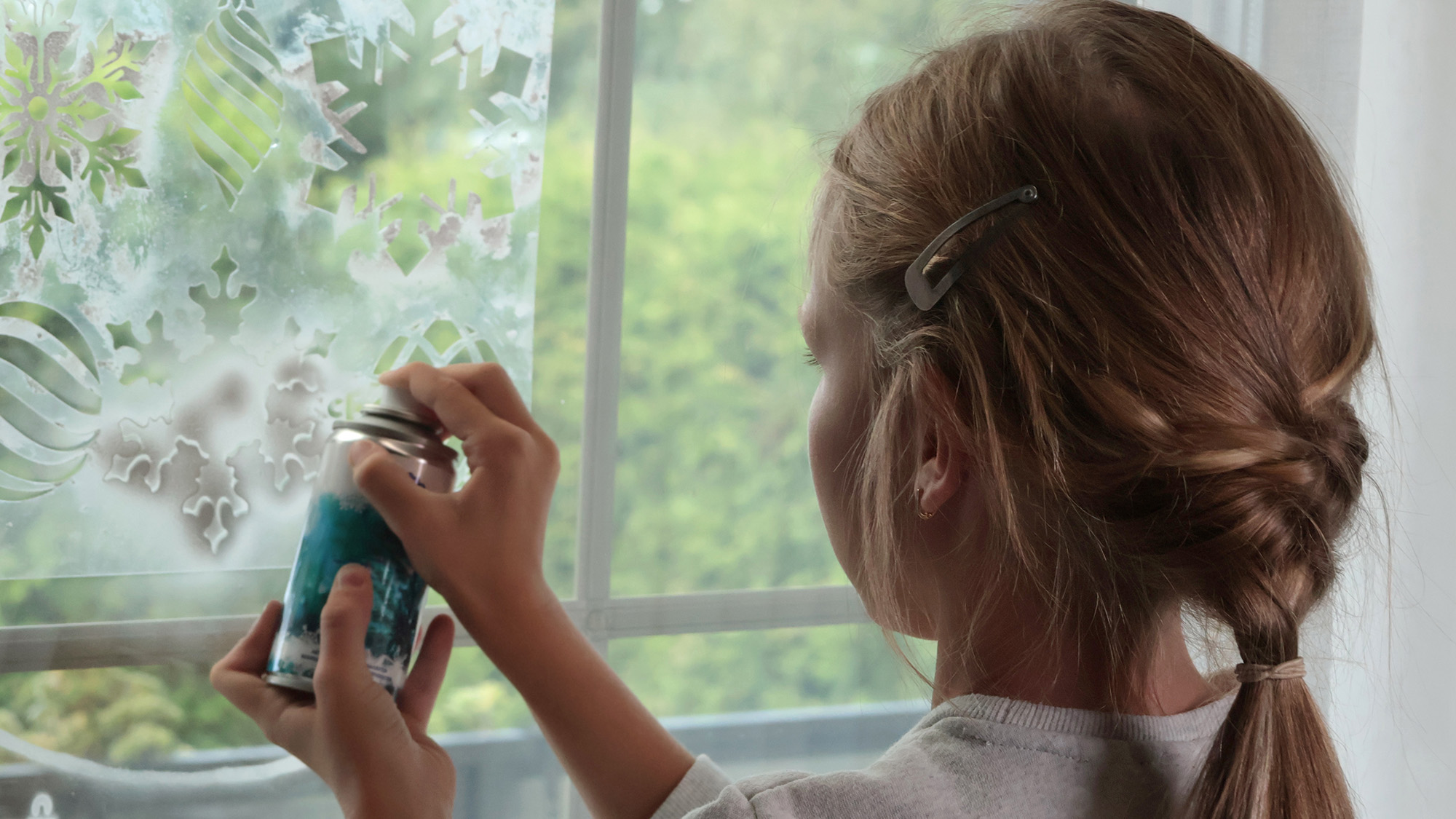 Child spraying artificial snow on window pane