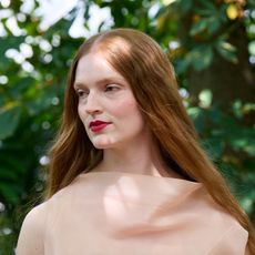 woman with red hair wearing a nude top in front of a tree