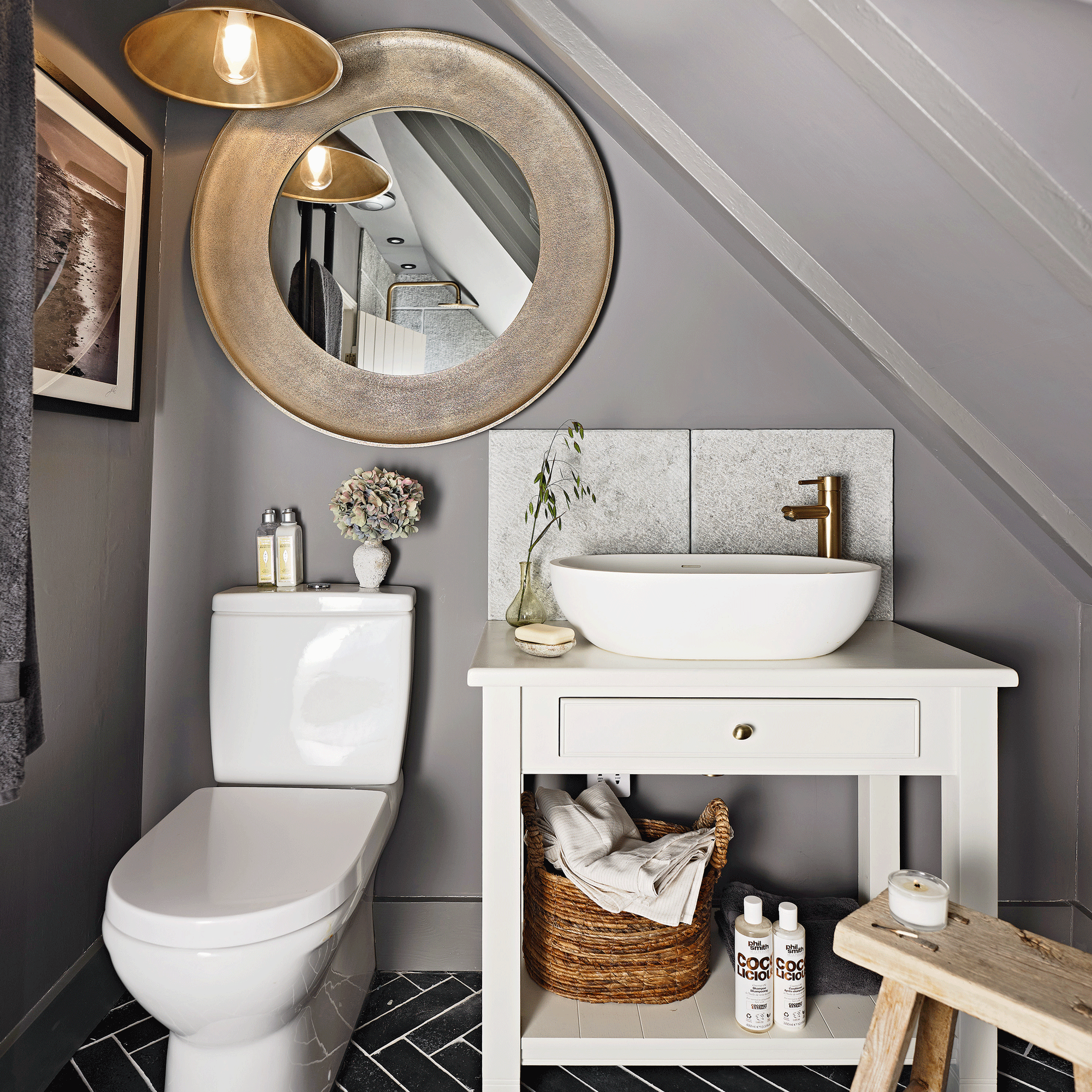 a bathroom in an loft room with white look and basin vanity a large round mirror and grey walls