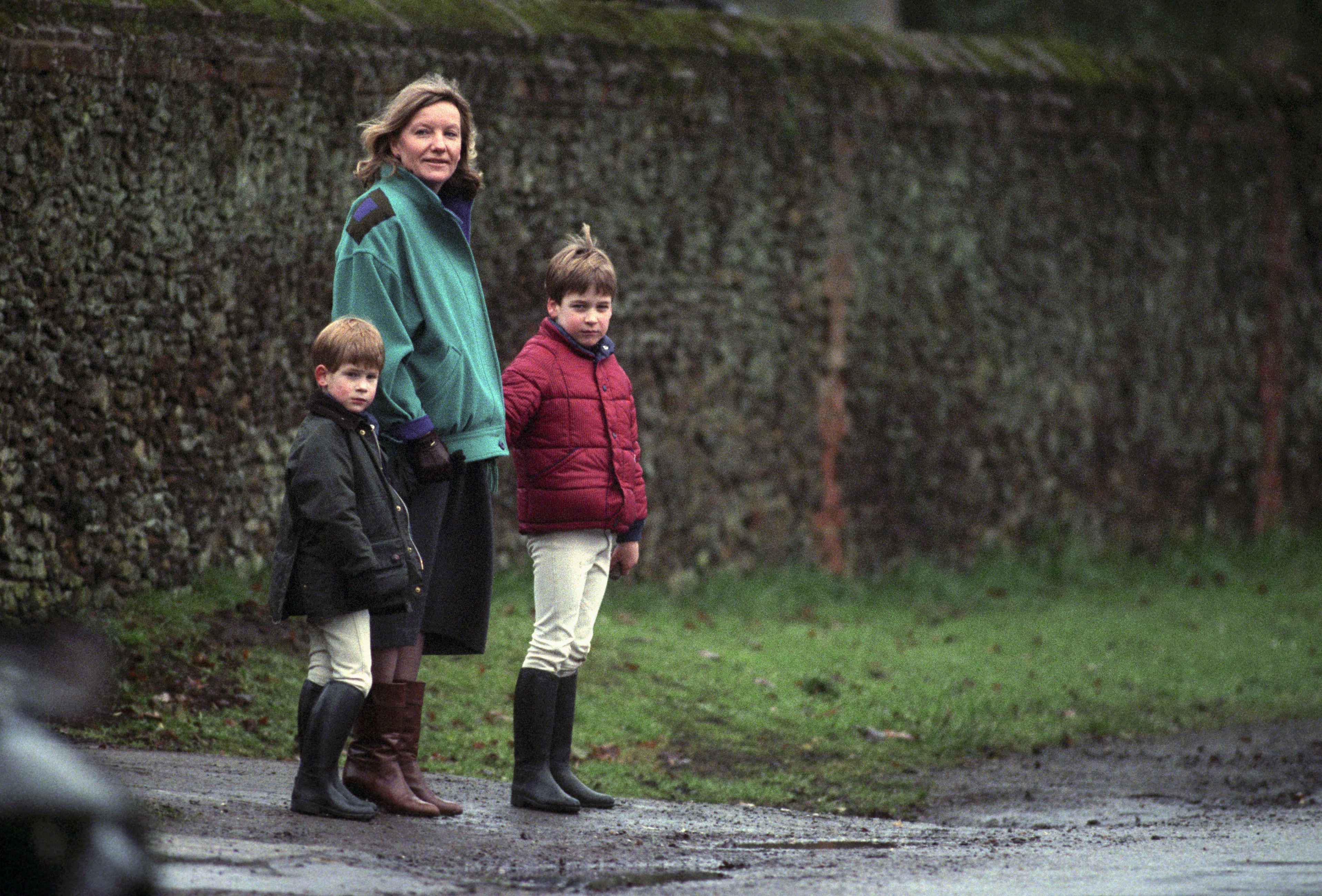 Prince William and Prince Harry standing with their nanny in front of an ivory-covered wall