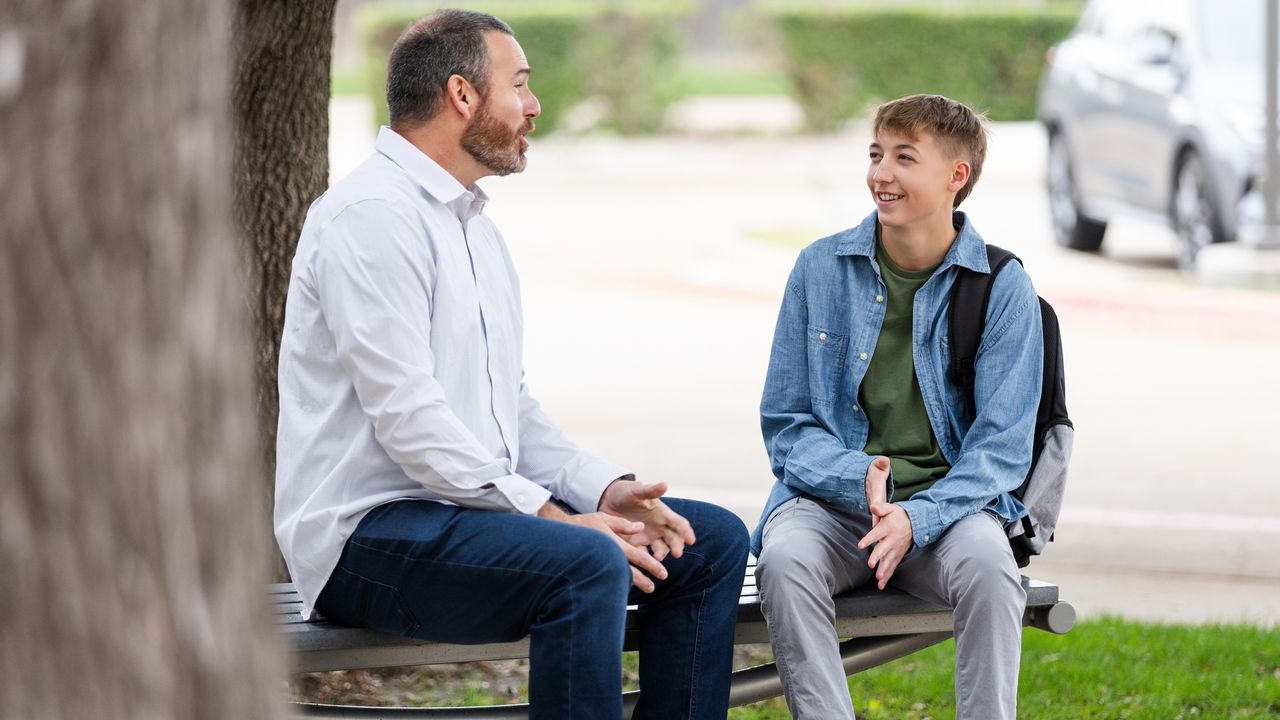 A dad and his son sit outside on a bench and talk.