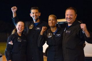 four people in dark flight suits smile and pump their fists