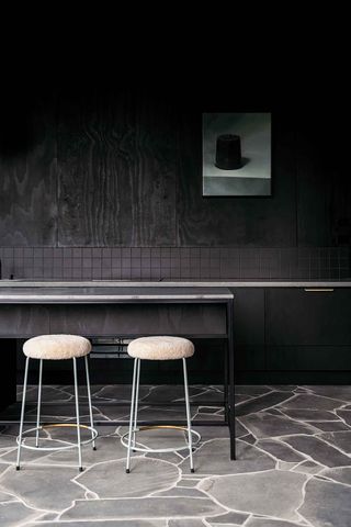 Dining area with a bench, two cream-coloured stools and black-stained walls with black tiles