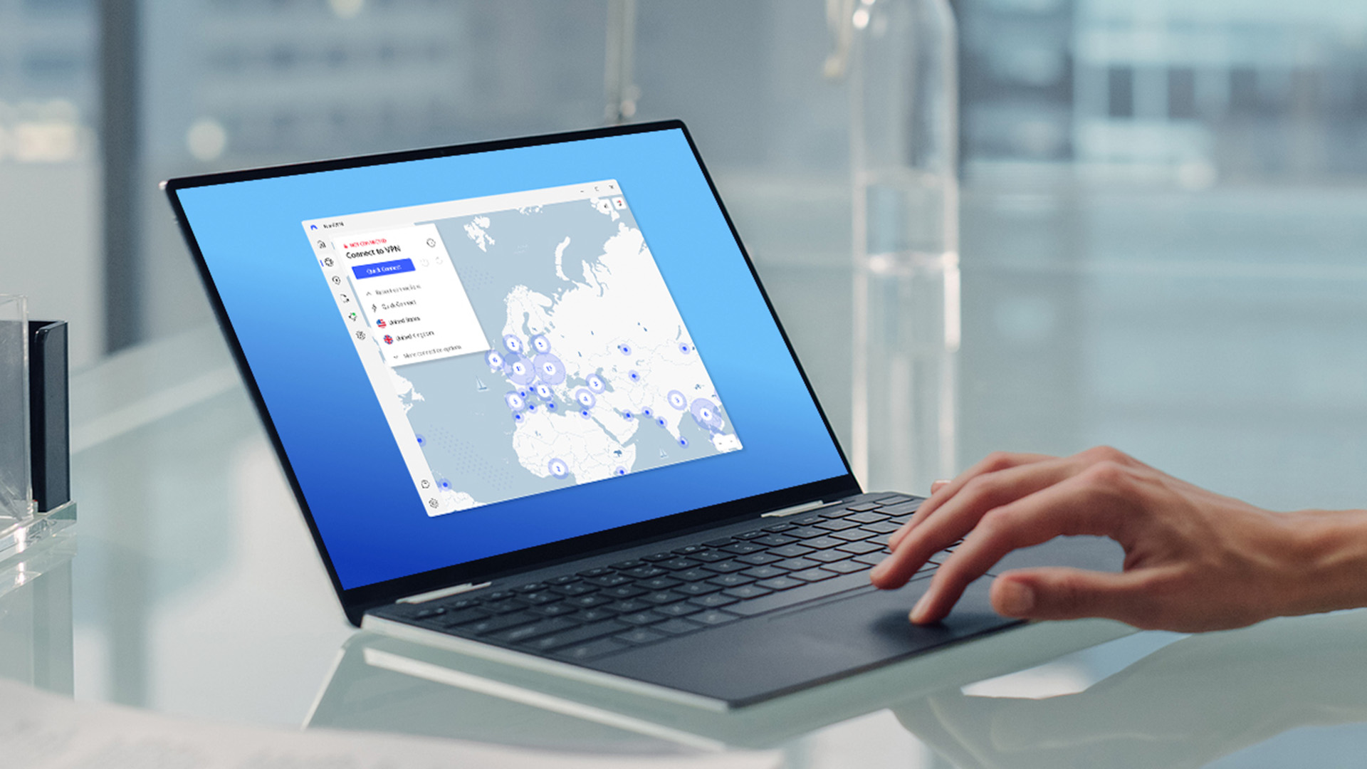 A hand touches a laptop trackpad as the device sits on a glass table, and the screen displays NordVPN