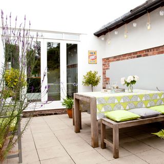 Courtyard garden, by wooden garden bench and table with lime green patterned cloth and cushions, stone concrete patio