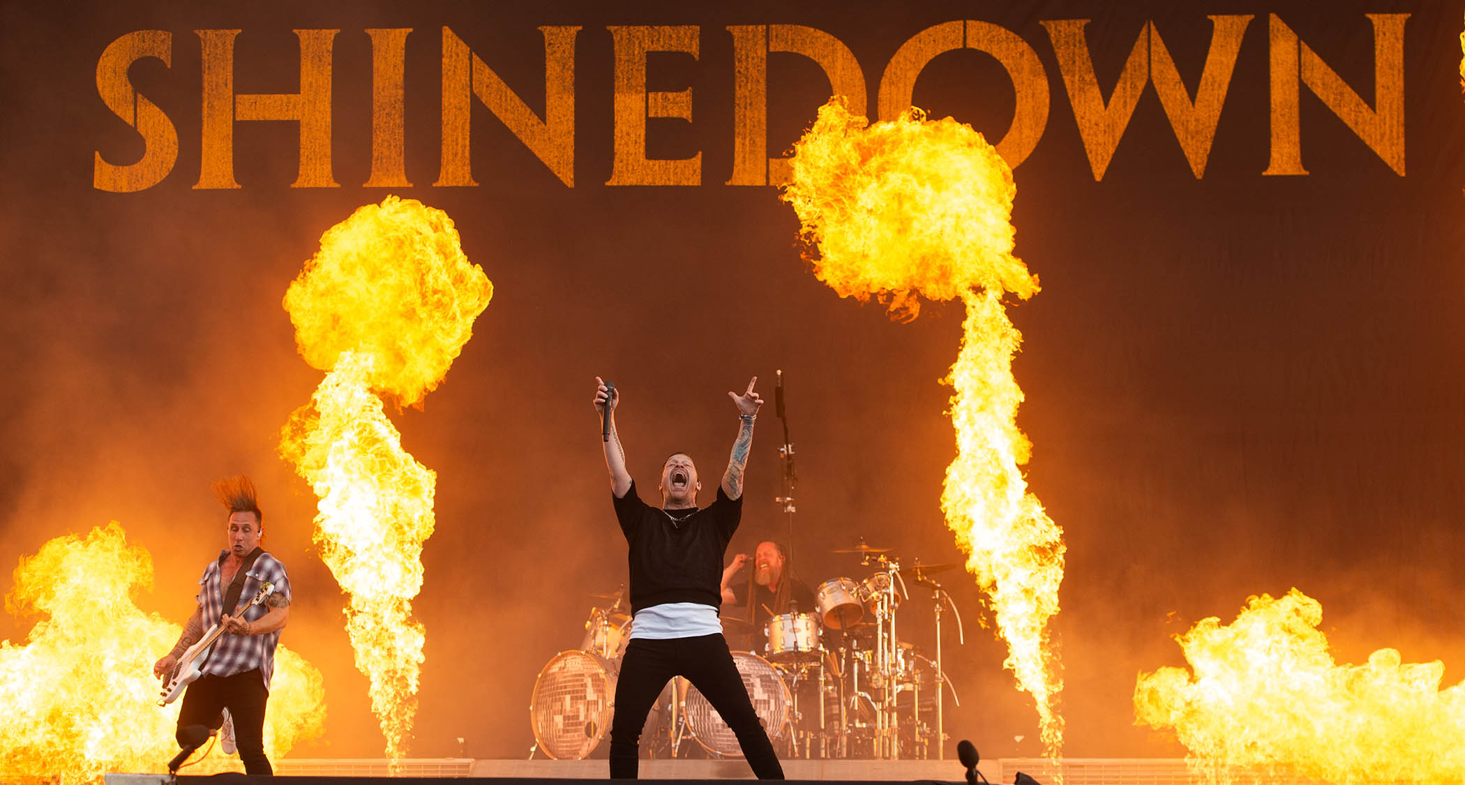 Shinedown perform on a Download Festival stage light up in orange from pyro. Frontman Brent Smith holds his hands in the air.