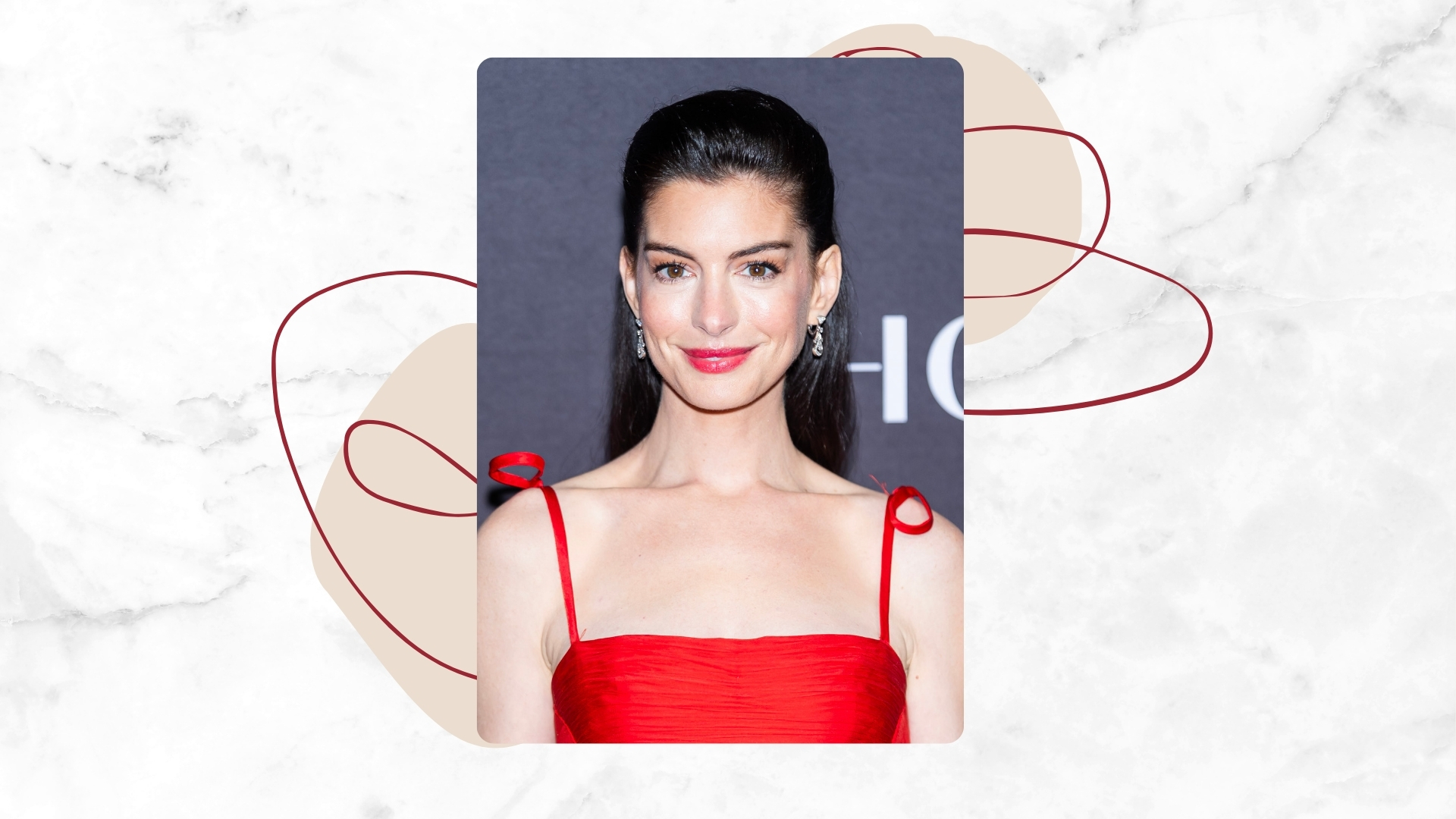 Image of Anne Hathaway smiling with straight brunette hair scraped back, wearing a red dress and red lipstick, on a white marble background with red and beige motifs