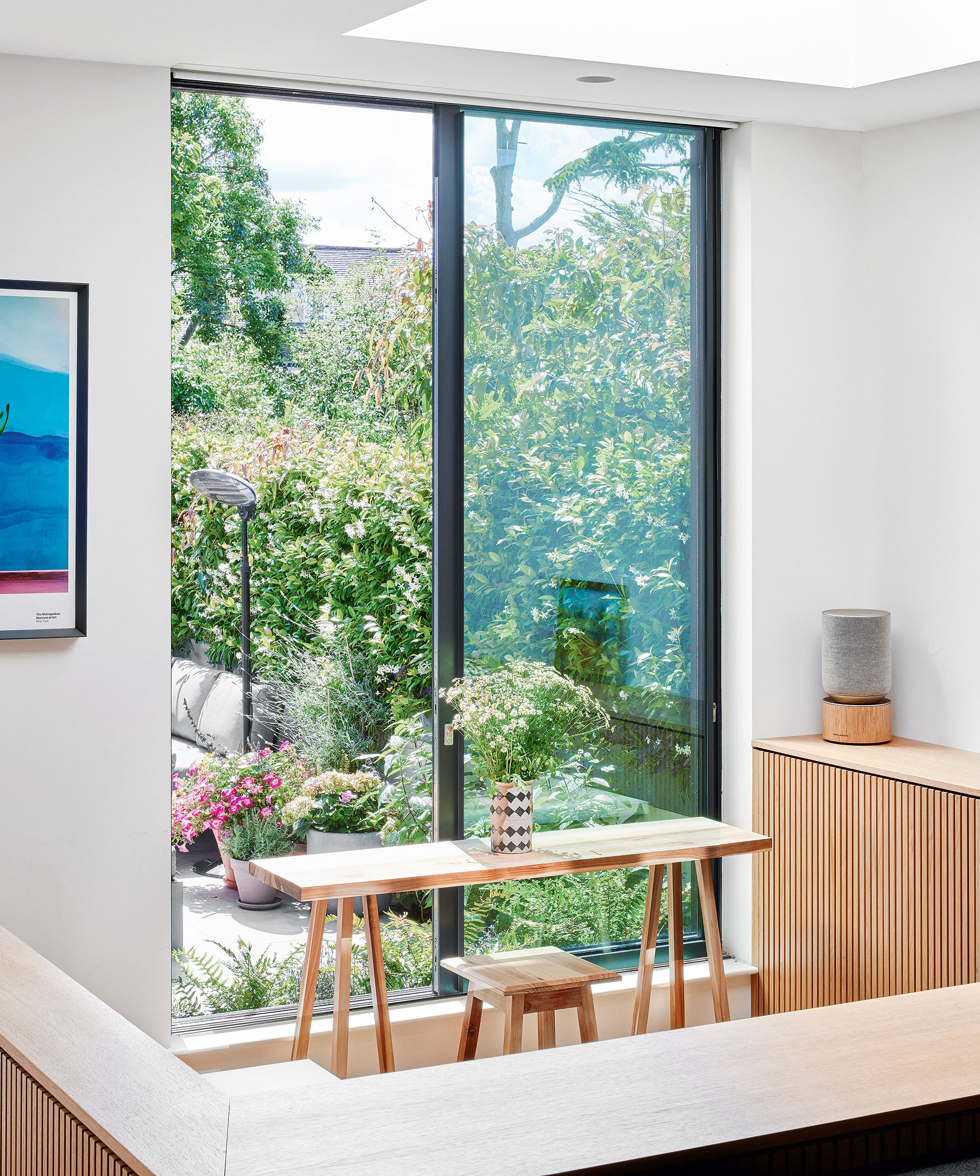 small home office area in an extended home with a wooden desk in front of a full-height window that overlooks the garden area