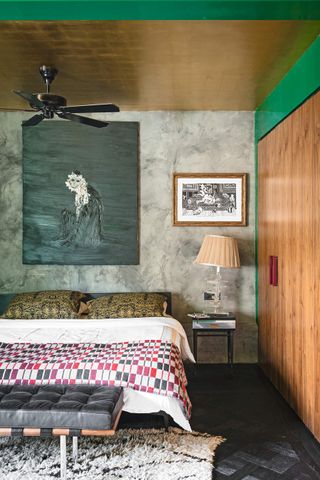 An eclectic bedroom with a gold foil ceiling, a ceiling fan and a large painted canvas above the bed