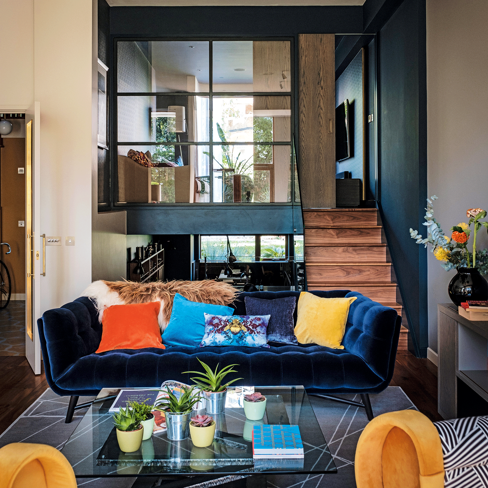 Black sofa with coloured cushions in front of glass clad mezzanine