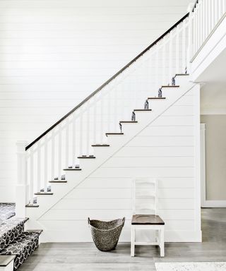 A staircase wit white shiplap walls and a black and white patterned carpet