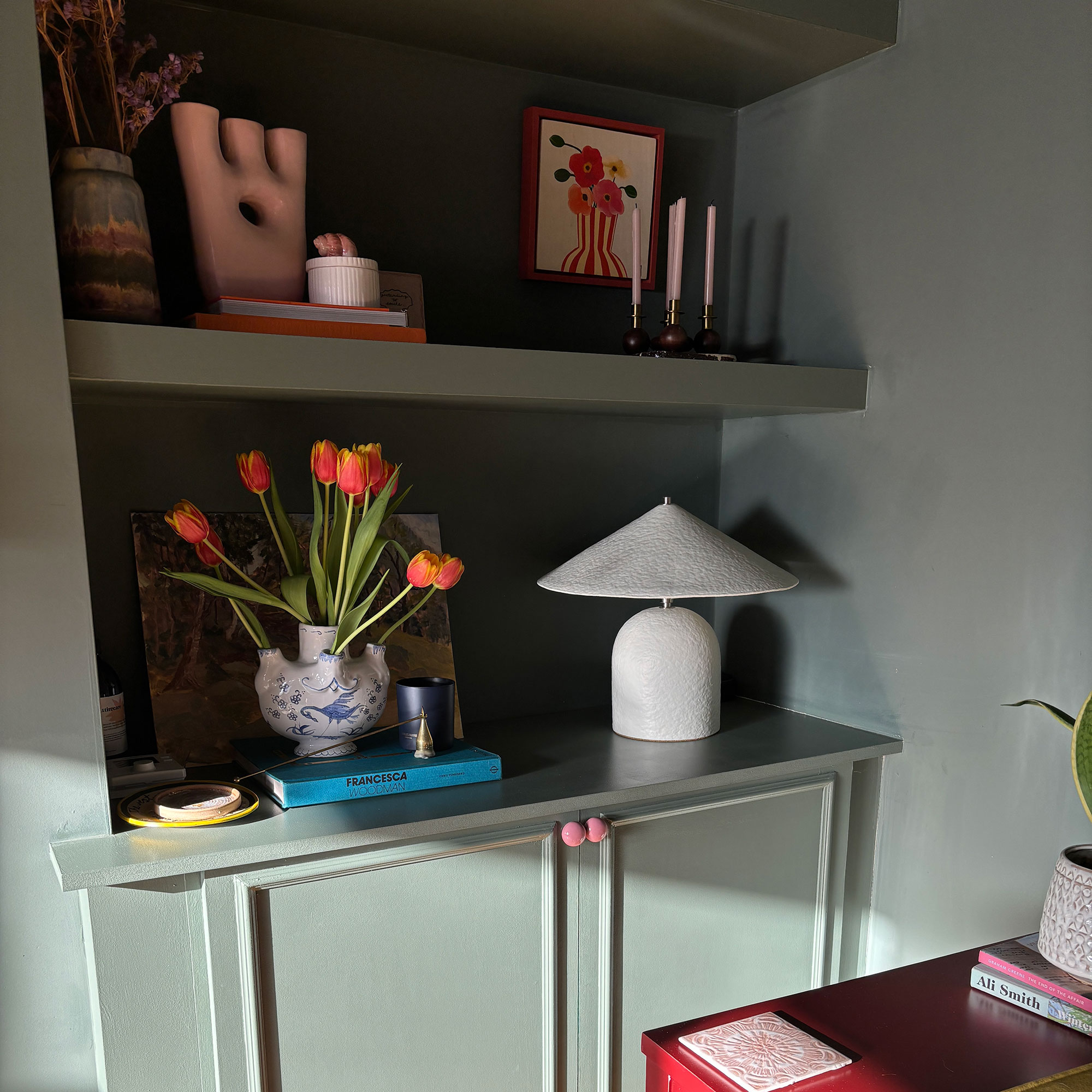 Green built-in shelving until with flowers, vases, books and table lamp